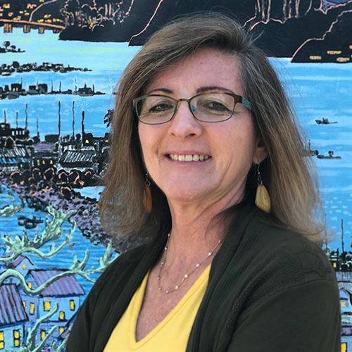 Photo of Trustee Bennet, yellow blouse, black sweater, blue background